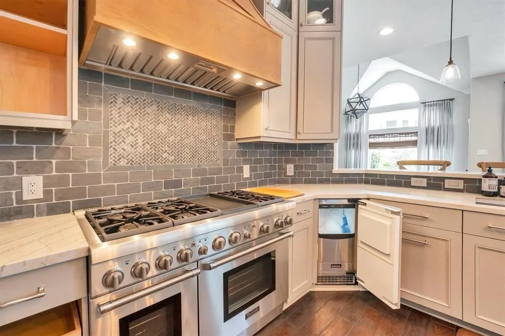 Professional gas range under a wood hood with a gray brick backsplash and herringbone tile inlay