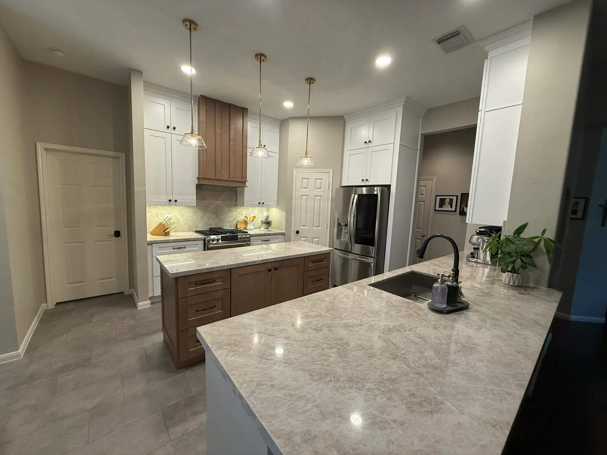 Remodeled kitchen with white shaker cabinets, a stained wood range hood, wood-tone island and quartzite countertops