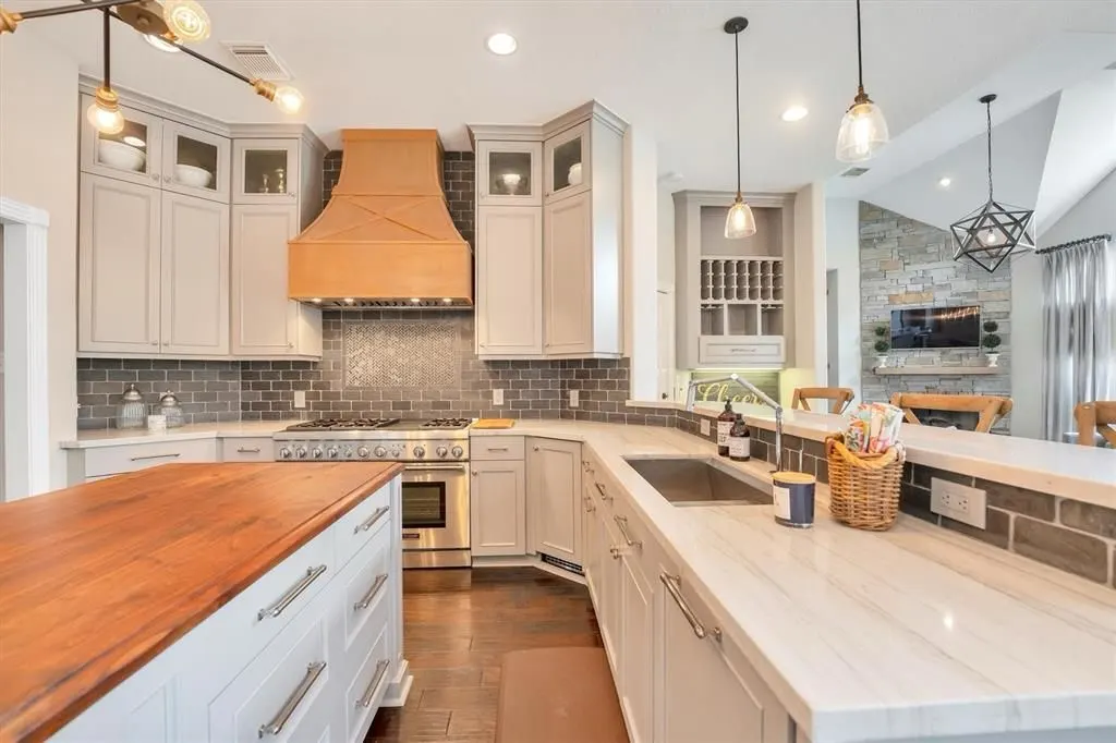 Remodeled kitchen with greige shaker cabinets, a natural wood range hood, gray brick backsplash and a butcher-block island